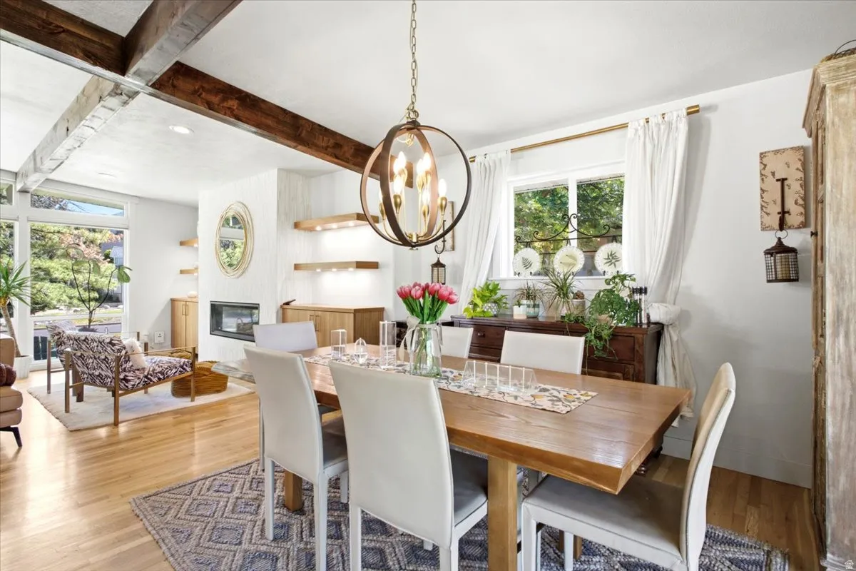 Open-concept dining and living area featuring exposed wood beams, wood-finish flooring, and a linear fireplace