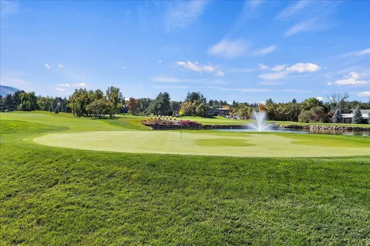 Expansive golf course green with manicured turf, a water feature with a fountain, and mature landscaping