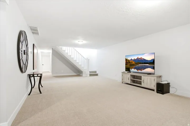 Spacious carpeted room featuring a white staircase with balusters, recessed lighting, and white baseboards