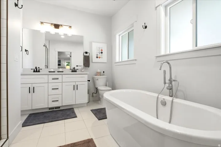 Bathroom featuring a freestanding soaking tub with a floor-mounted faucet, a double vanity with white cabinetry and dark hardware, a large wall mirror, and tiled flooring