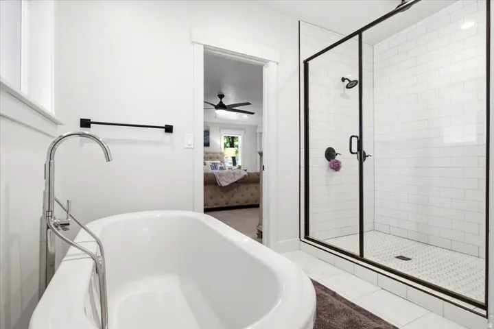 Freestanding soaking tub with a floor-mounted chrome faucet, alongside a glass-enclosed shower featuring subway tile surround, hexagon tile flooring, and matte black fixtures