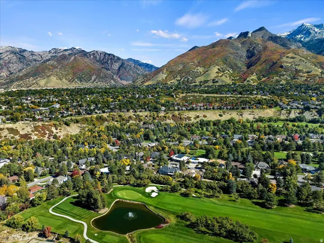 Aerial perspective showcasing a verdant golf course with a central pond and water feature, surrounded by mature trees and residential properties