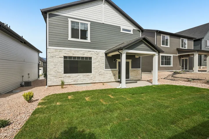Exterior featuring board and batten siding, stone facade, covered patio, and a manicured lawn