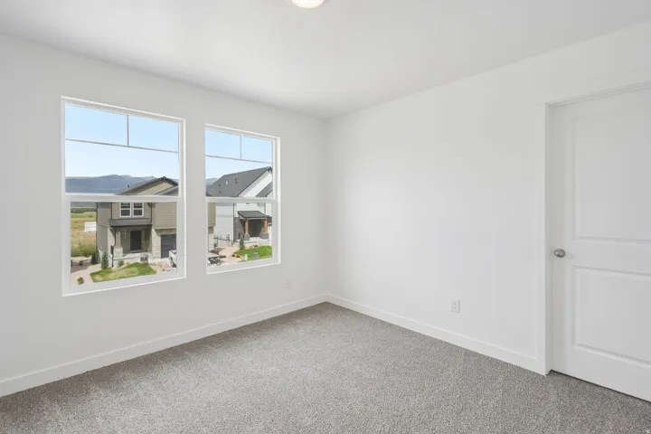Neutral wall paint, two white-framed windows, and gray carpeted flooring