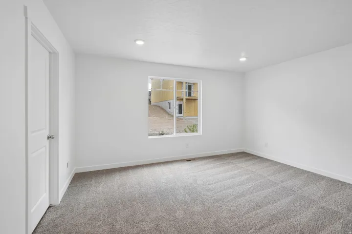 Recessed lighting, neutral wall tones, gray patterned carpet, and a white interior door