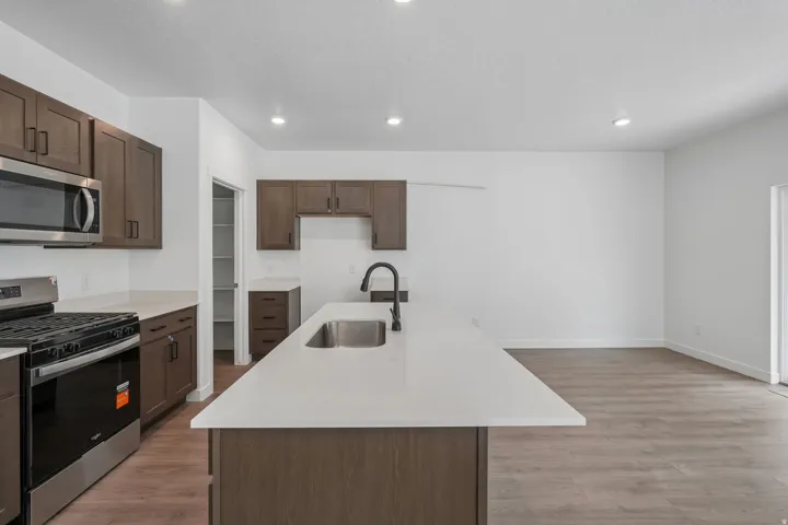 Kitchen featuring wood-finish cabinetry, stainless steel appliances, a center island with sink, light-toned countertops, and recessed lighting