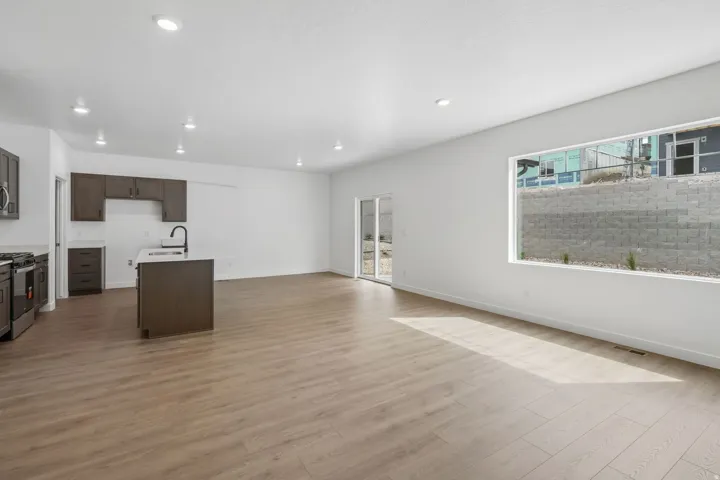 Open-concept living space featuring wood-finish flooring, recessed lighting, a kitchen island with a black gooseneck faucet, dark wood cabinetry, and a large horizontal window