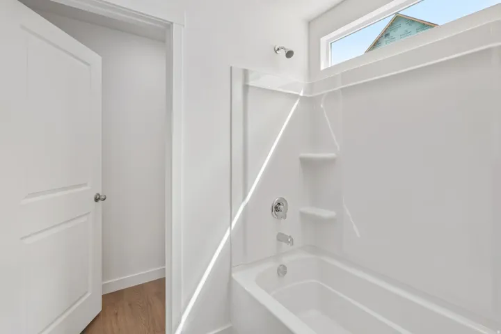 Bathtub with integrated shower surround, chrome fixtures, and transom window