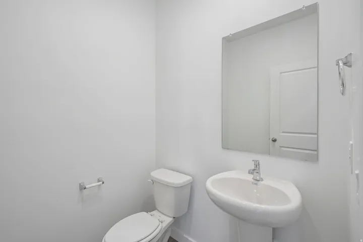 Pedestal sink with chrome faucet, wall-mounted mirror, and white toilet
