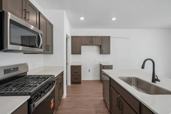 Modern kitchen featuring stainless steel appliances, dark wood-finish cabinetry, light-toned countertops, wood-finish flooring, and recessed lighting