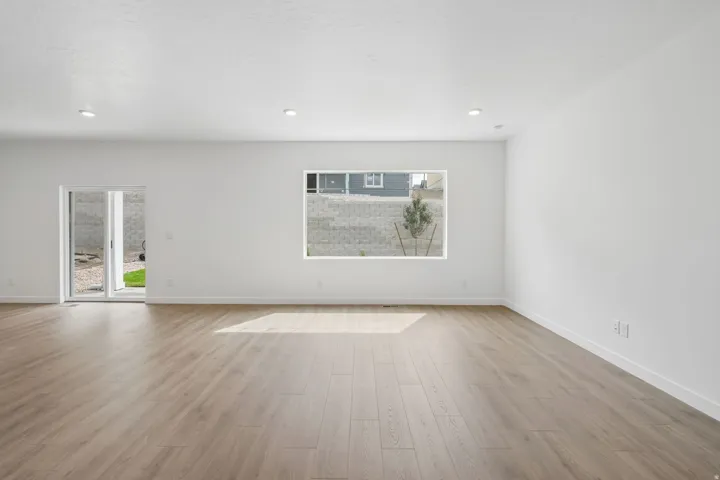 Spacious room featuring wood-finish flooring, recessed lighting, a large window, and glass sliding doors
