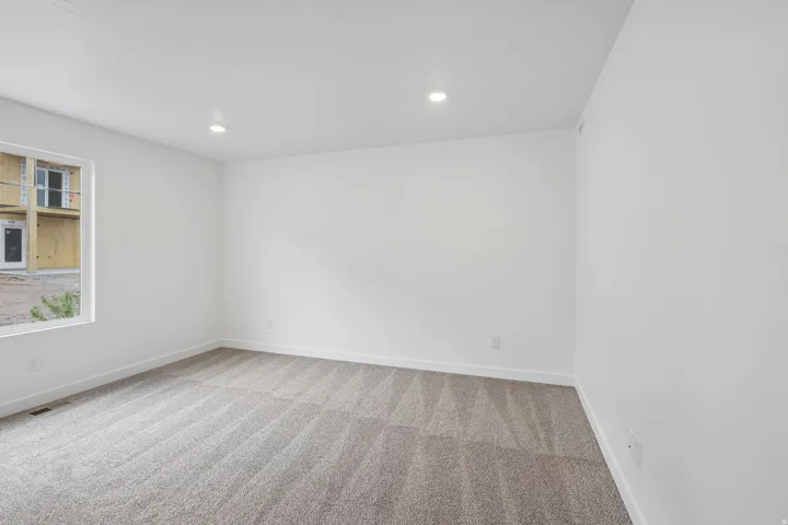 Recessed ceiling lighting, neutral carpeting, window with natural light, white walls