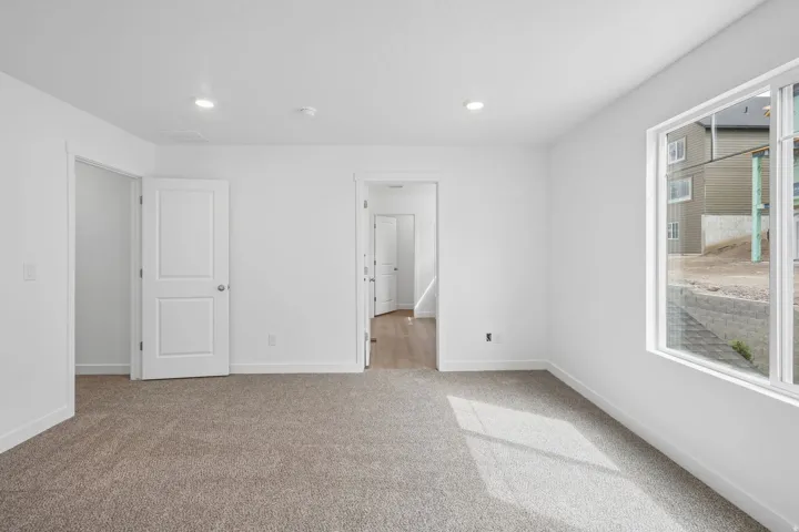 Neutral tone carpeting, recessed ceiling lighting, a large window, and white interior doors