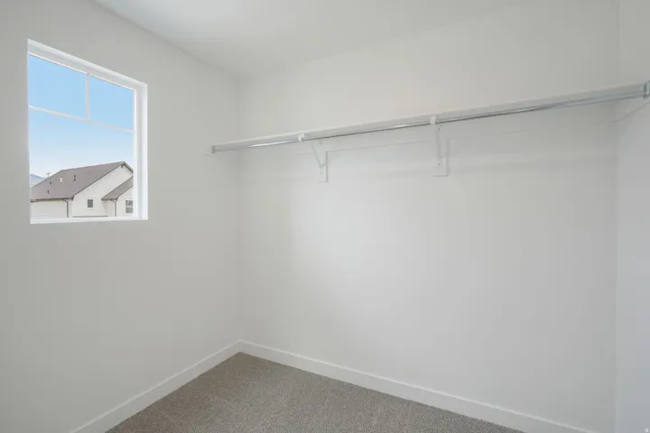 White walls, gray carpet, and a single window with a built-in hanging rod