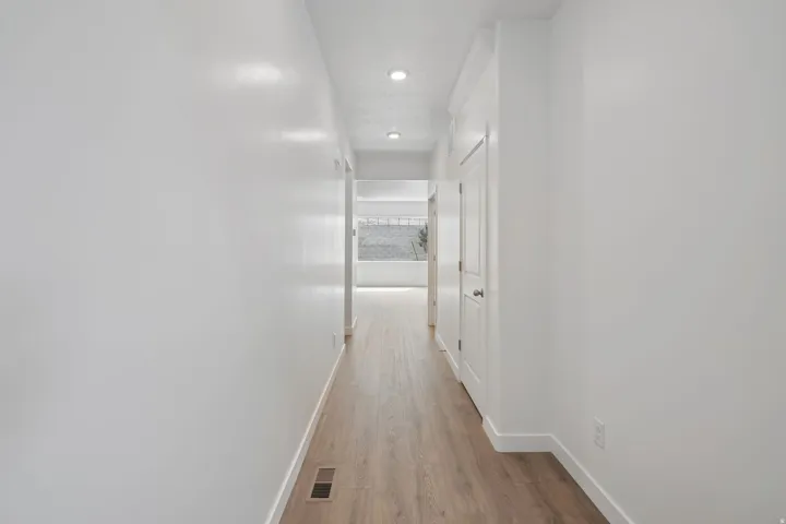 Hallway featuring wood-finish flooring, white walls, recessed lighting, and a white door with a circular knob