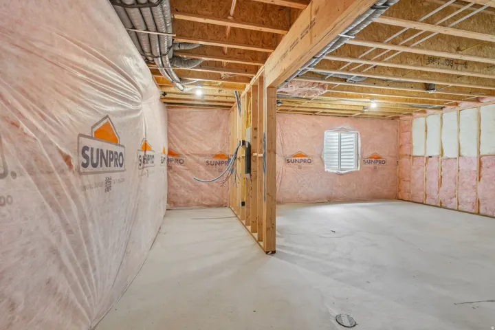 Unfinished basement featuring exposed wood framing, concrete flooring, insulated walls, and a visible window opening