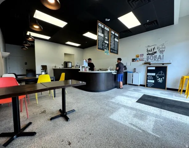Contemporary commercial interior featuring a curved service counter, dark wood-finish tables, and speckled composite flooring