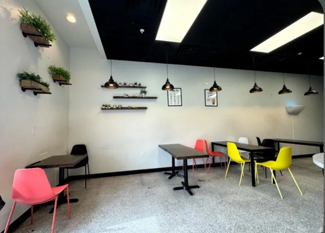 Commercial interior featuring a speckled floor, white walls, and a black ceiling with recessed and suspended lighting