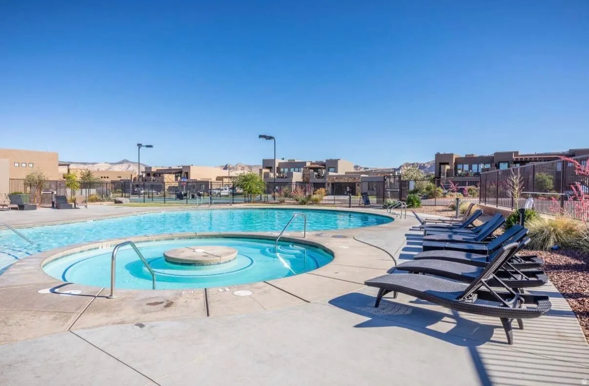 Community swimming pool featuring a connected spa, surrounding concrete deck, and perimeter fencing