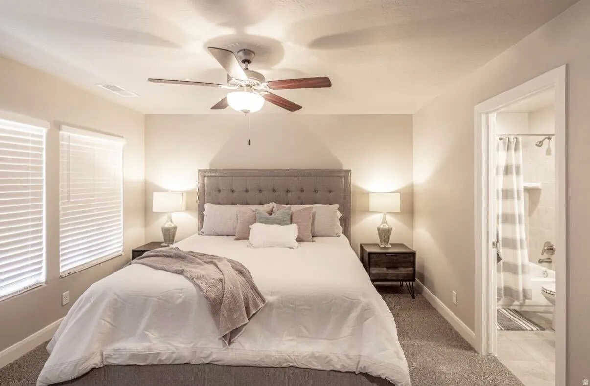 Spacious bedroom with neutral-toned walls, two large windows with blinds, and a ceiling fan with integrated lighting