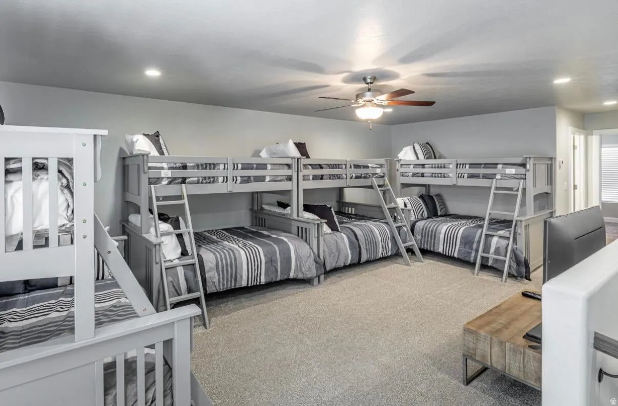 Spacious room featuring four bunk beds with grey wood-finish frames, plush carpet flooring, a ceiling fan, and recessed lighting