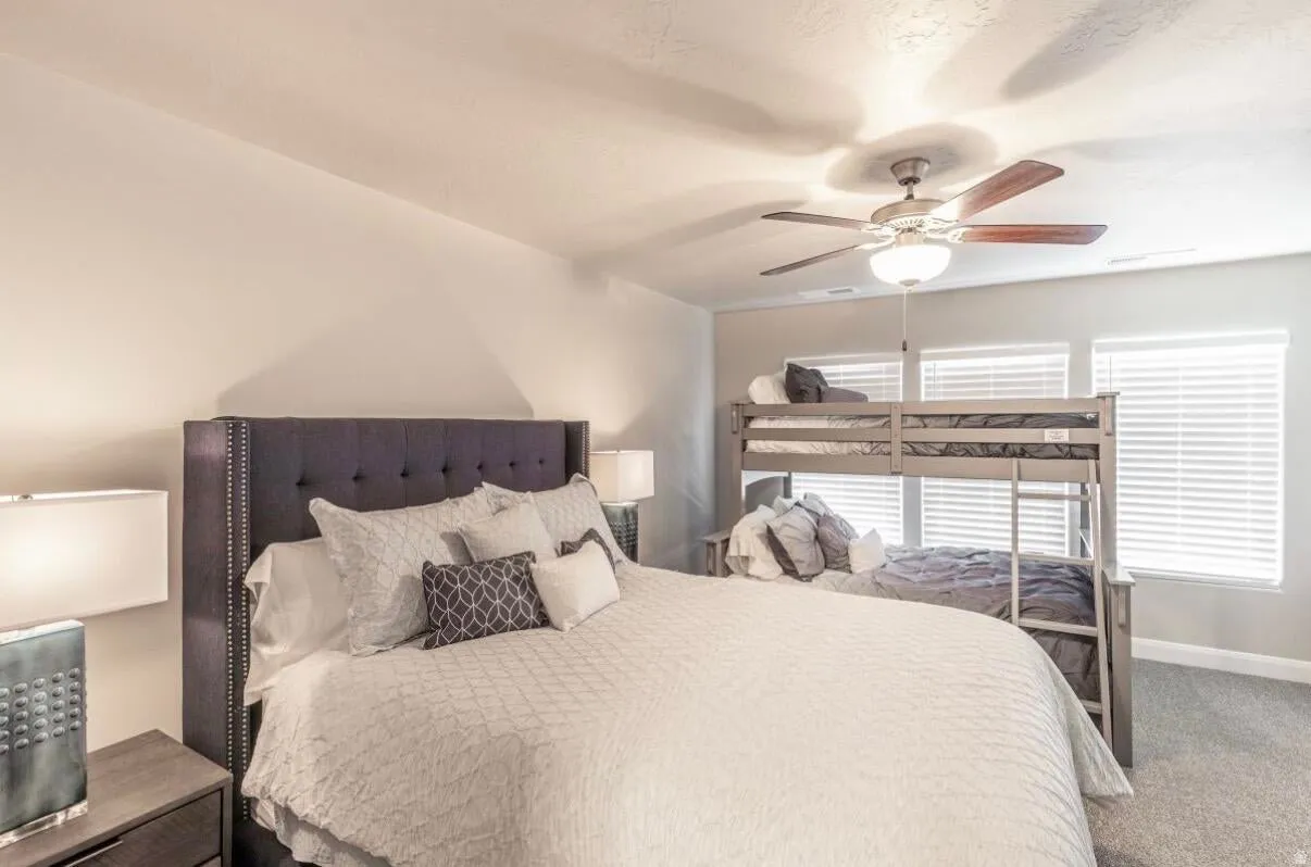 Spacious room featuring light gray wall paint, textured carpet flooring, and a ceiling fan with integrated lighting