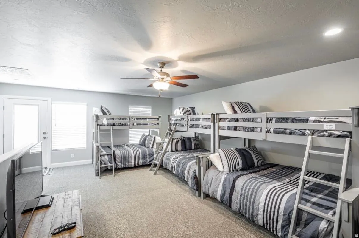 Spacious room featuring multiple bunk beds, neutral tone carpeting, a ceiling fan, recessed lighting, and a white door with an adjacent window