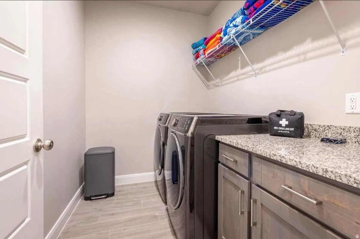 Dedicated laundry area featuring wood-finish flooring, light gray walls, a built-in wire shelf, and a granite-style countertop with dark wood cabinetry