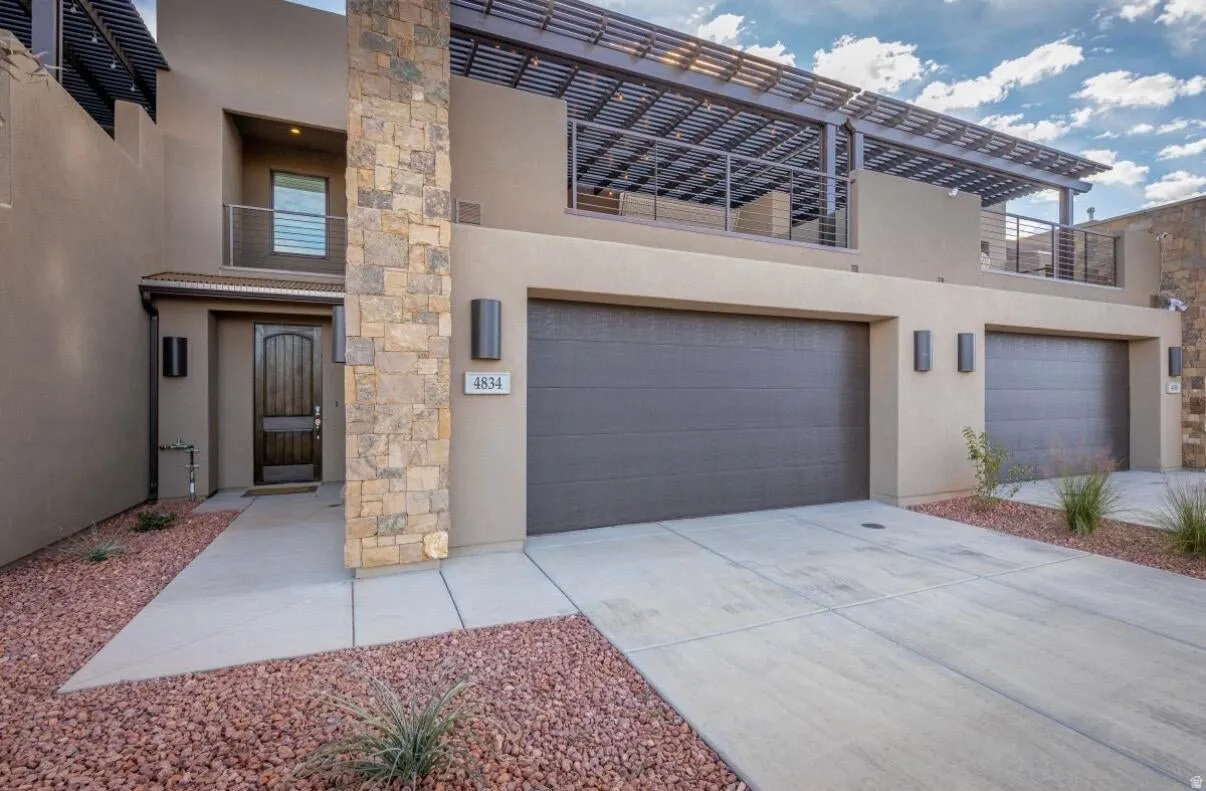 Contemporary exterior featuring dual garage doors, a stone-clad pillar, and a second-story patio with a pergola