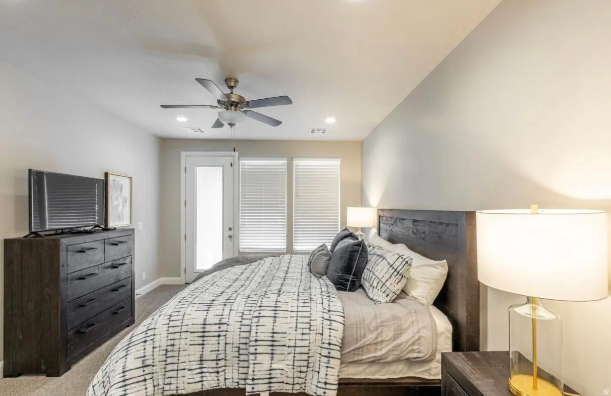Carpeted bedroom featuring a ceiling fan, recessed lighting, a door with a glass insert, and two windows with blinds