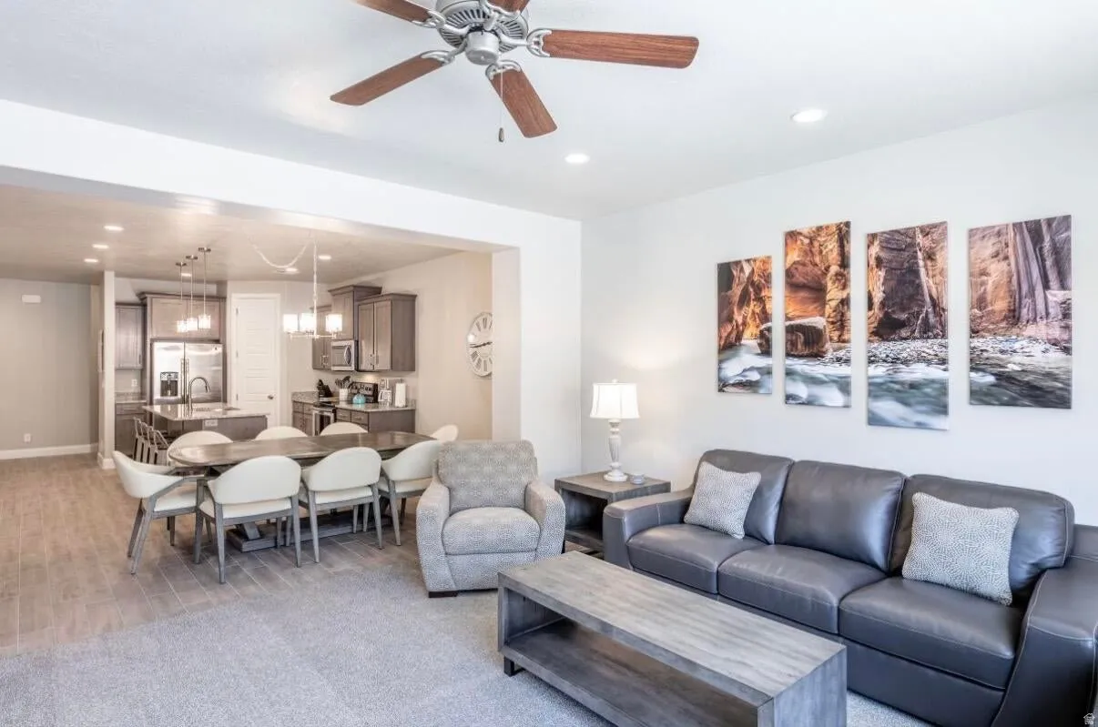 Open-concept living area featuring a ceiling fan with wood-finish blades, recessed lighting, and mixed flooring with carpet and wood-finish planks
