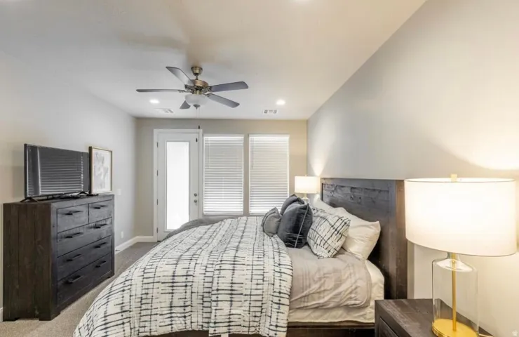 Carpeted bedroom featuring a ceiling fan, recessed lighting, a door with a glass insert, and two windows with blinds
