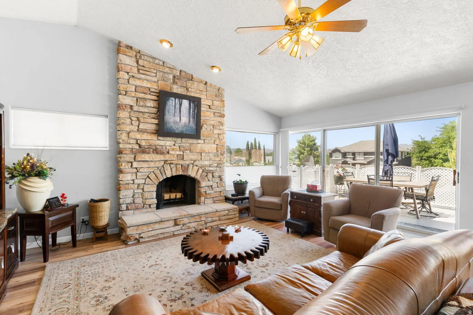 Living area featuring a floor-to-ceiling stone fireplace, vaulted ceilings with recessed lighting, wood-finish flooring, and sliding glass doors opening to an outdoor patio space