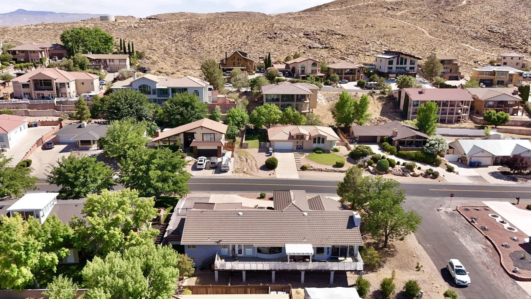 Property featuring a tiled roof, an extensive elevated deck with white railing, and mature landscaping
