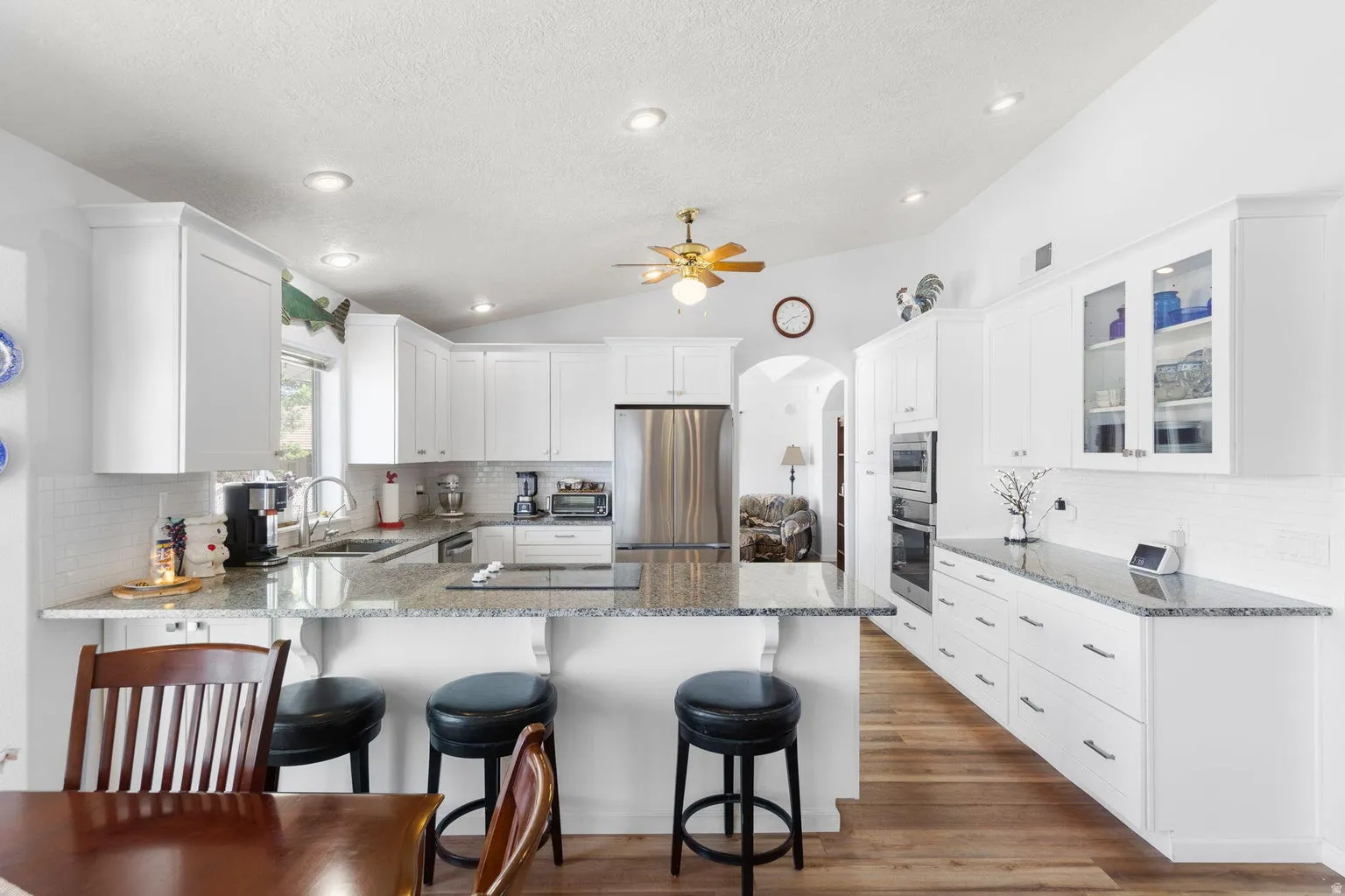 Bright kitchen featuring white cabinetry, granite countertops, stainless steel appliances, a tile backsplash, and wood-finish flooring