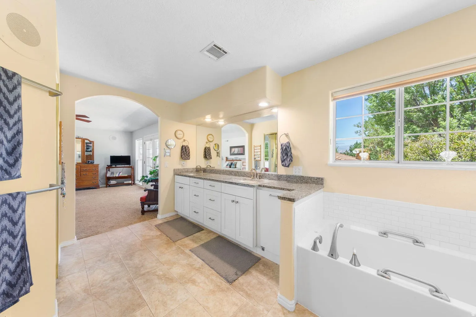 Bathroom featuring a dual vanity with a speckled countertop, a built-in bathtub with white subway tile surround, arched entryway, and tile flooring