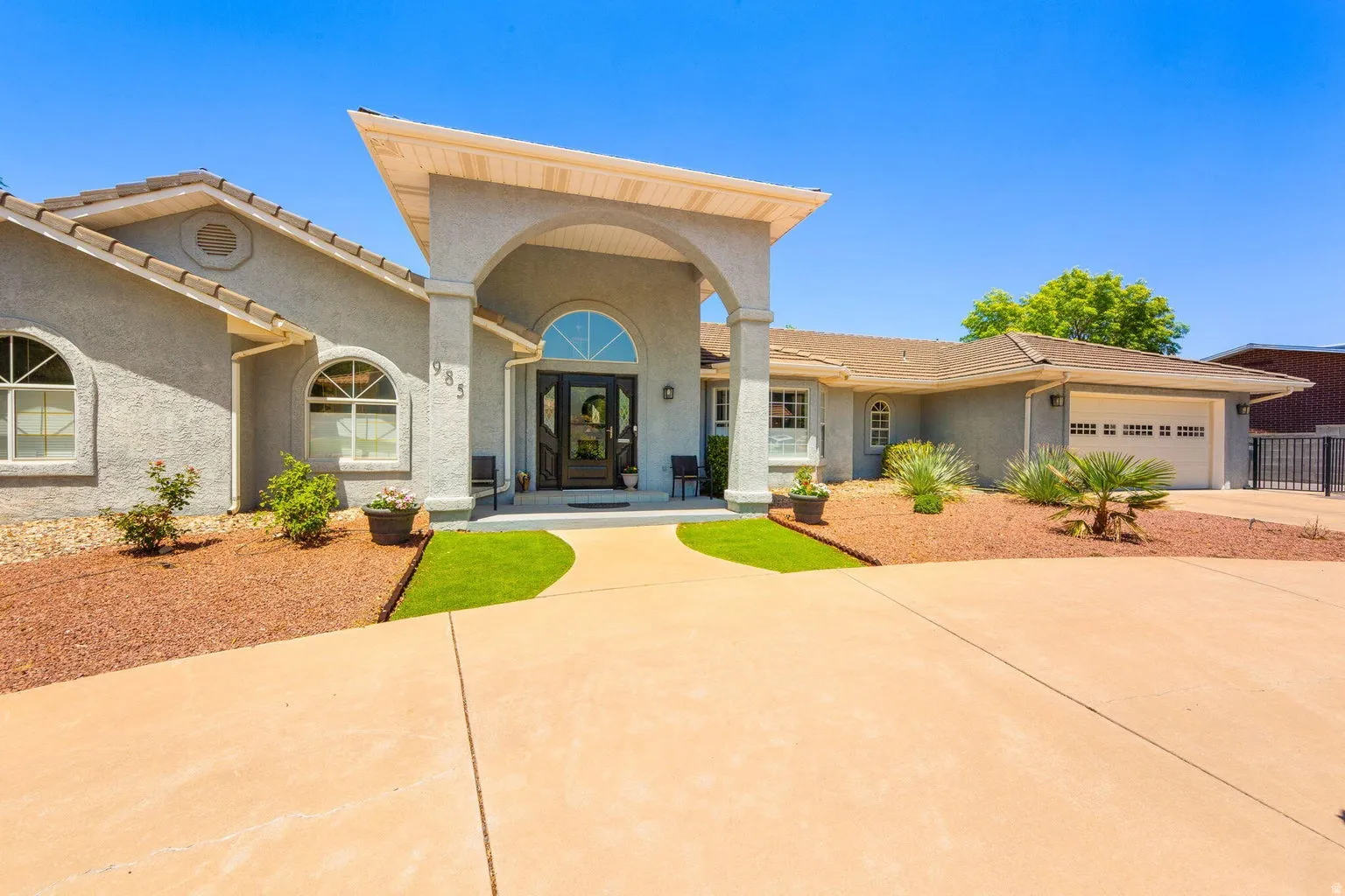 Stucco exterior featuring an arched portico entry with a transom window, arched windows, an attached two-car garage, and a concrete driveway