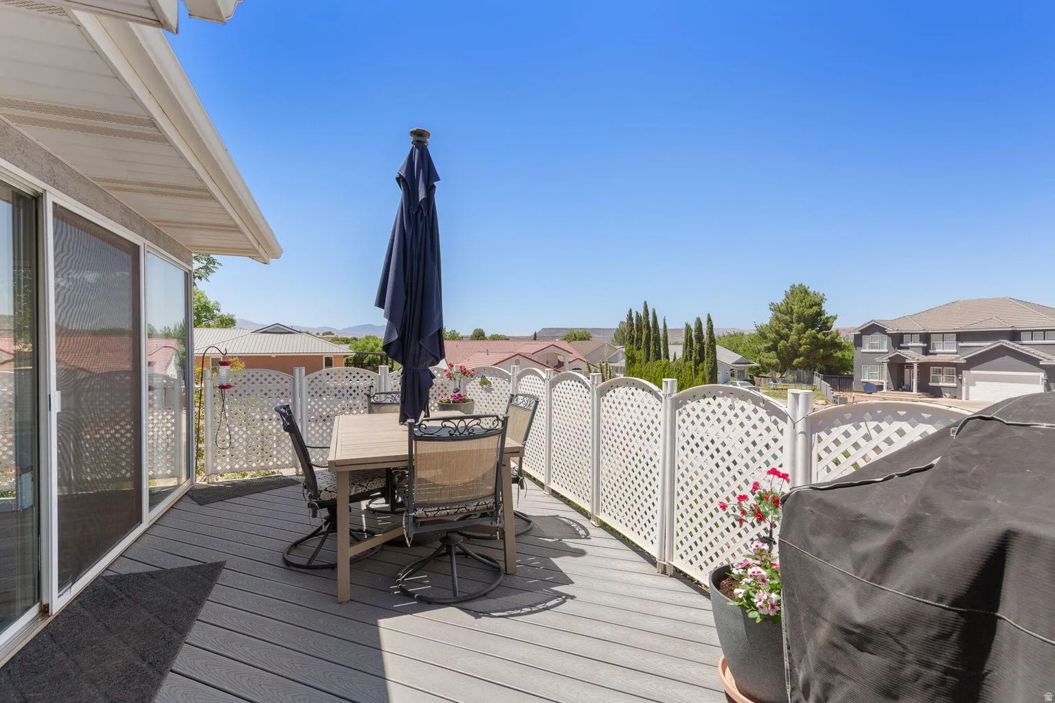 Expansive outdoor deck featuring wood-finish flooring, white lattice fencing, and a full-length sliding glass door