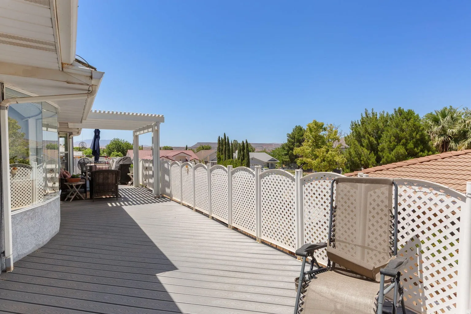 Expansive outdoor deck featuring wood-finish flooring, a white lattice fence, and a pergola providing partial shade