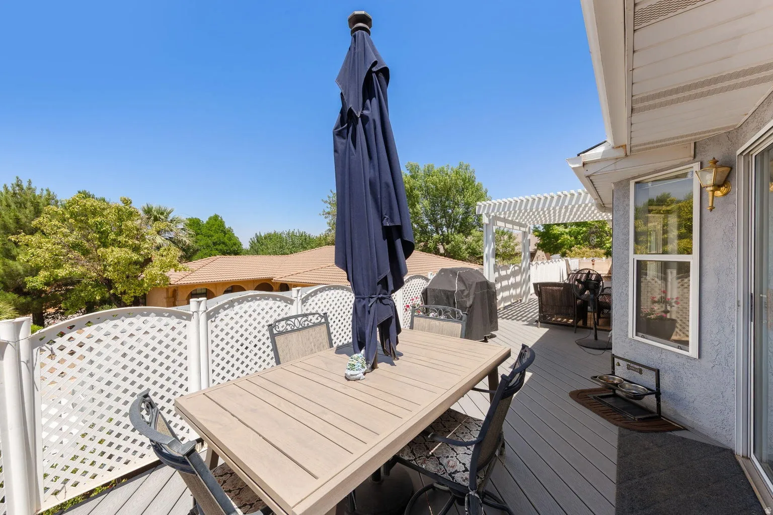 Spacious outdoor deck featuring composite decking, white lattice railing, a white pergola, and exterior wall lantern lighting