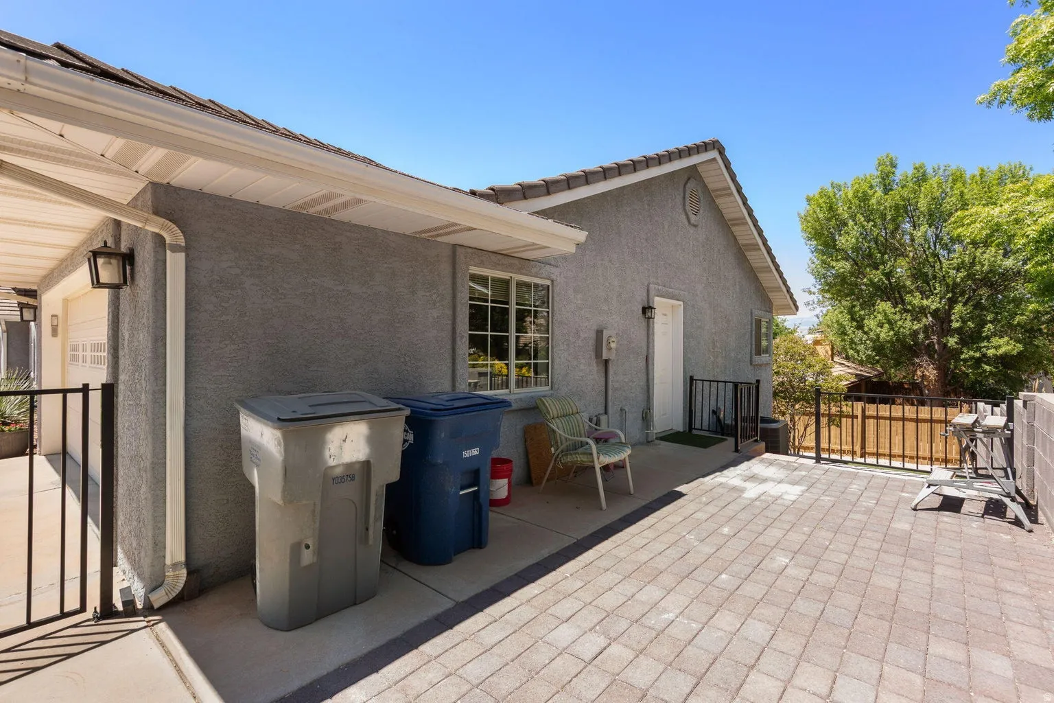 Paved patio area featuring light-toned paver stones, a stucco exterior, and a tiled roofline