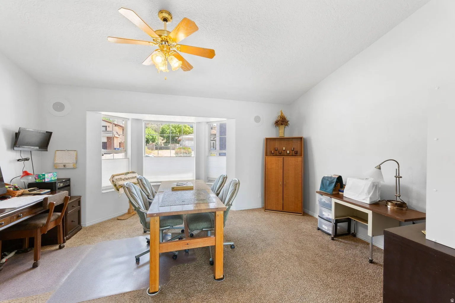 Bright room featuring a prominent bay window, neutral carpeting, and a ceiling fan with integrated lighting