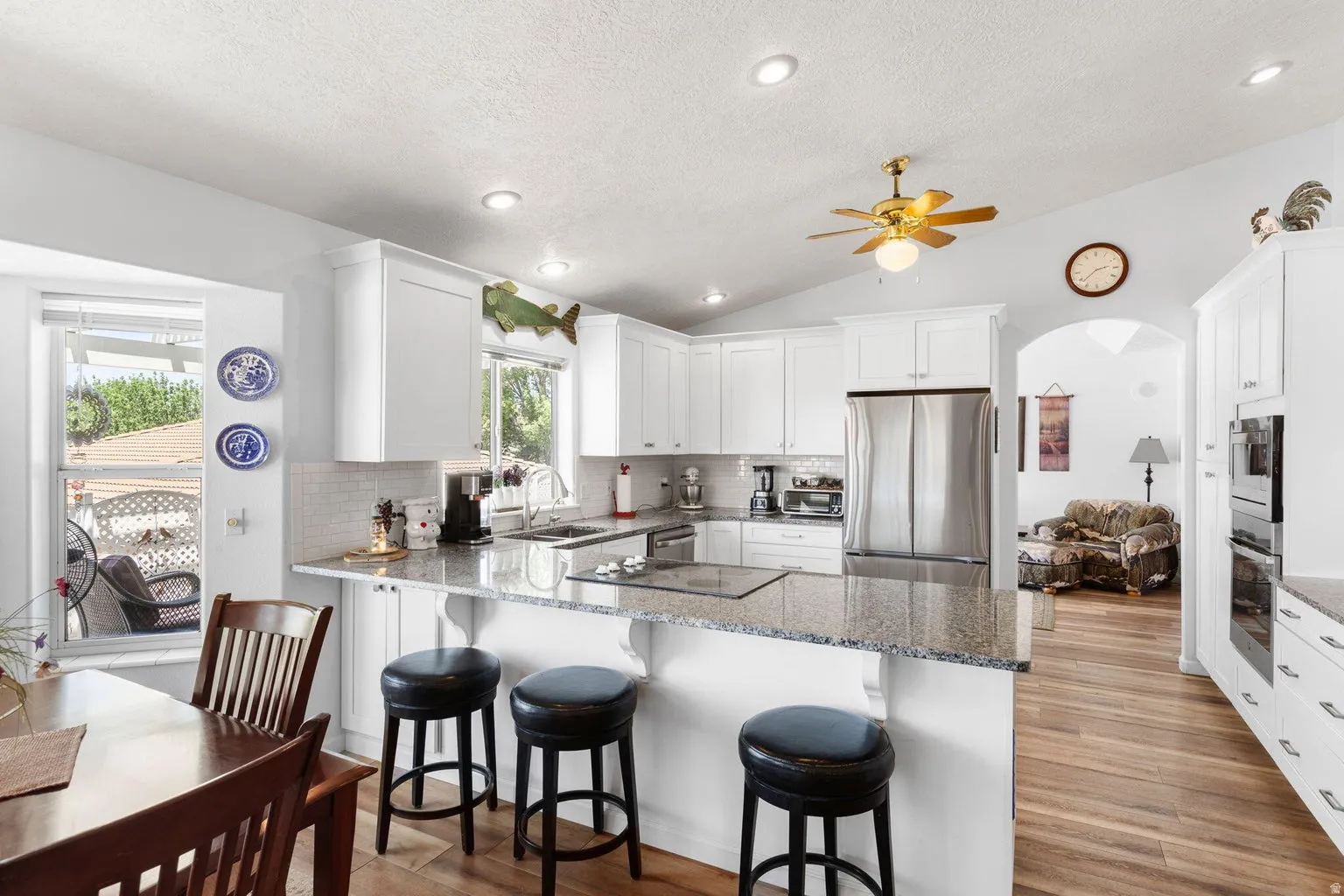 Open-concept kitchen featuring white shaker cabinetry, granite countertops, a built-in cooktop, and stainless steel appliances