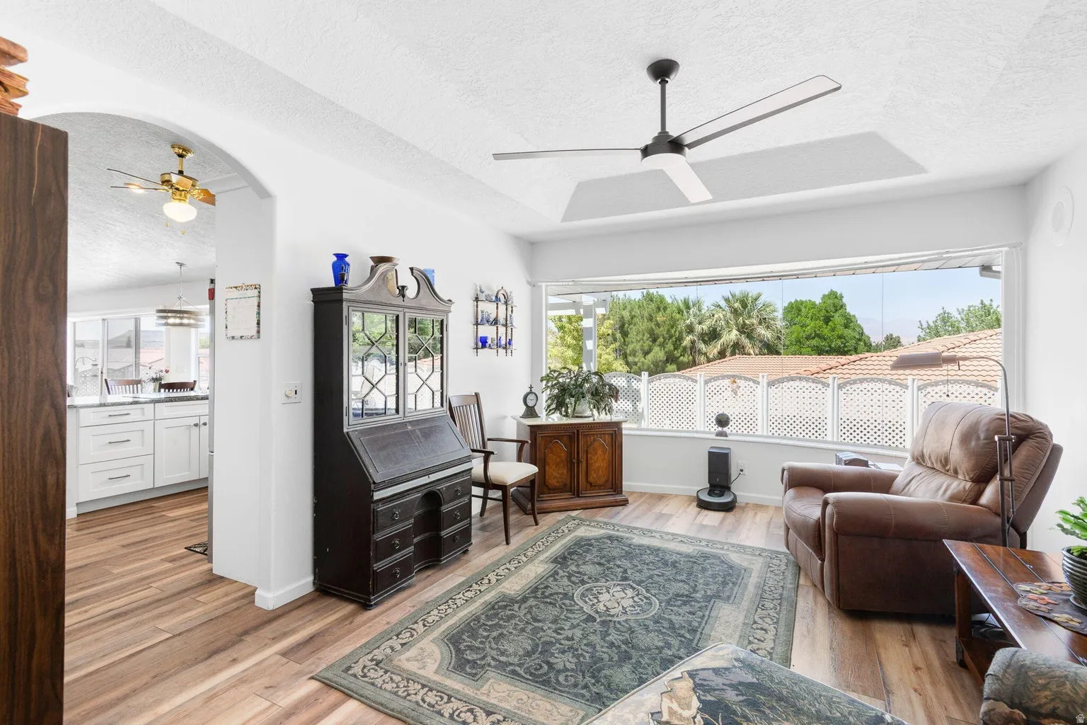 Living area featuring wood-finish flooring, a contemporary ceiling fan, and a wide window overlooking exterior landscaping