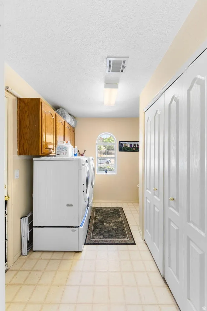 Laundry area featuring wall-mounted cabinetry, bi-fold closet doors, a curved arch window, and tile flooring