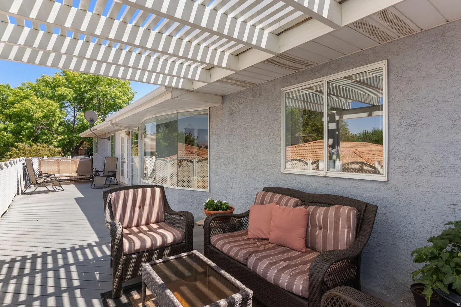 Expansive outdoor deck featuring a white slatted pergola, gray decking, and a white perimeter railing