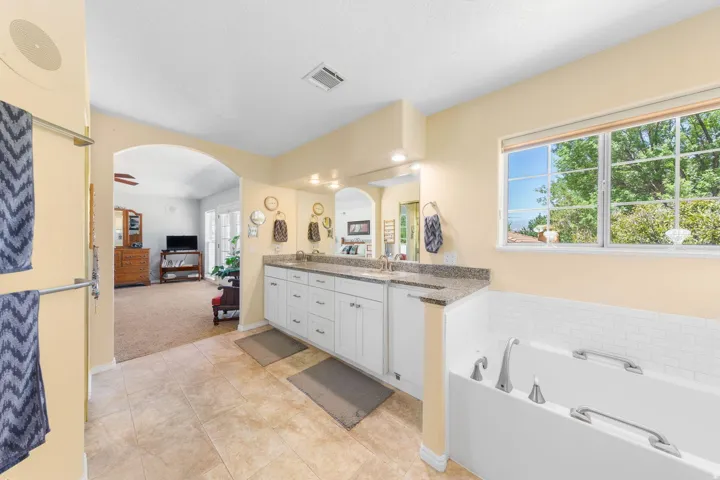 Bathroom featuring a dual vanity with a speckled countertop, a built-in bathtub with white subway tile surround, arched entryway, and tile flooring
