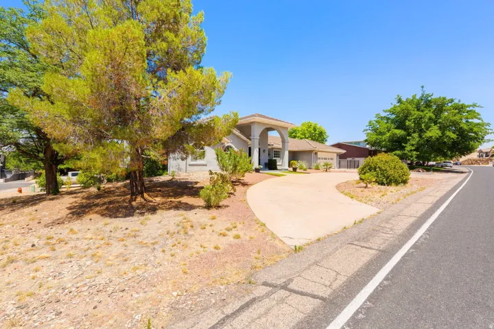 Traditional stucco exterior with a tiled roof, featuring an arched portico entryway, an attached two-car garage, mature trees, and a concrete driveway