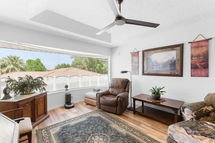 Wide window providing exterior views, wood-finish flooring, ceiling fan, white wall finishes, and a decorative console cabinet