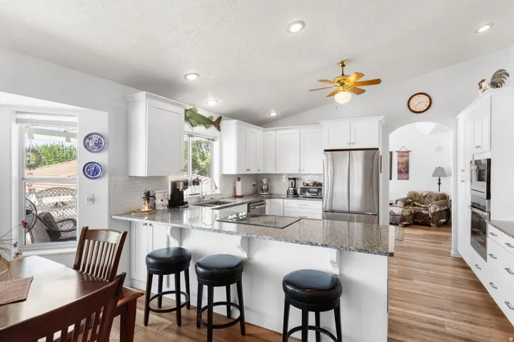 Open-concept kitchen featuring white shaker cabinetry, granite countertops, a built-in cooktop, and stainless steel appliances